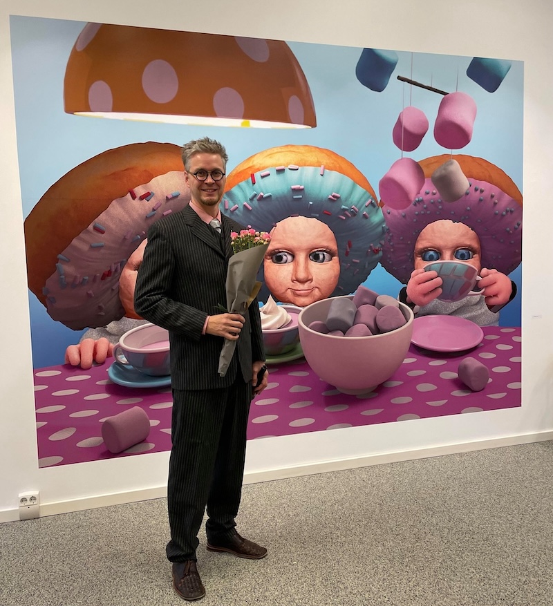 Sigurður Bragason stands in front of his colorful, creative art, holding a bouquet of flowers.