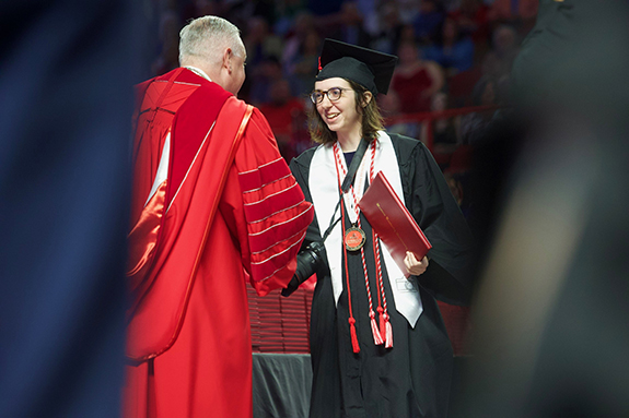 WKU graduate shaking hands with President Caboni while wearing cords, stoles, and Honors medallion