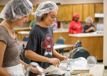 Two WKU students wearing hairnets cook in a food science lab.