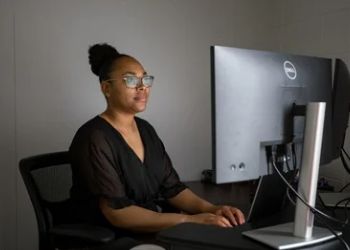 A person sits behind a desk and looks at a computer screen.