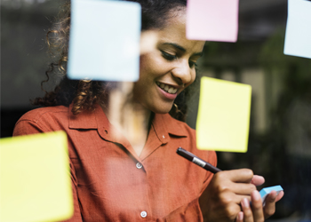 A person smiles and writes on a sticky note.