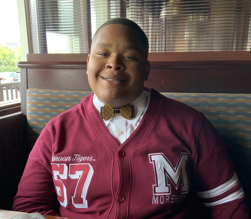 Richard sits in a restuarnt booth weearing a Morehouse jacket and a bow tie.