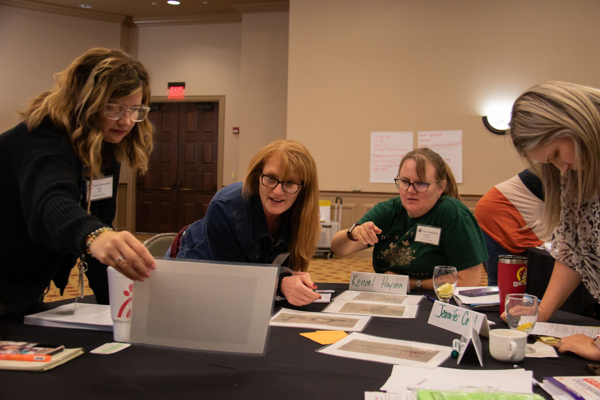 four women standing around a table smiling as they work together