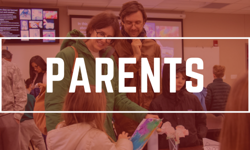 two parents smiling down at child showing their painting.