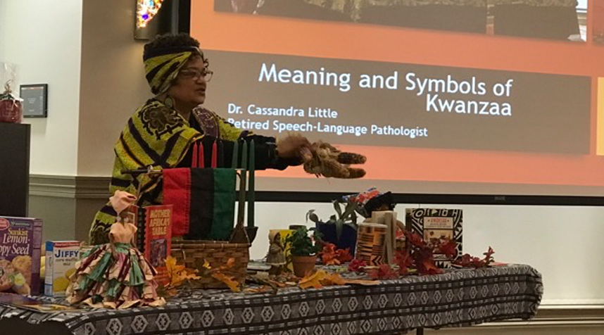 Woman presenting corn in front of a table of food at a Kwanzaa celebration
