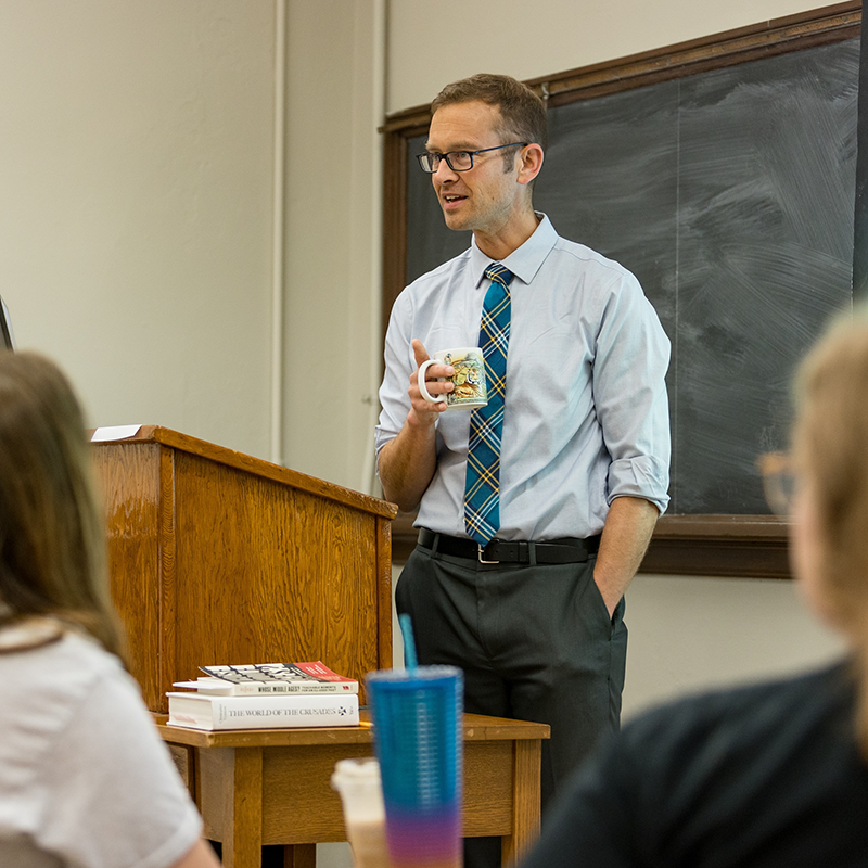 Man holding a coffee cup giving a lecture.