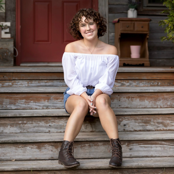 Woman with curly brown hair sitting on steps looking happy.