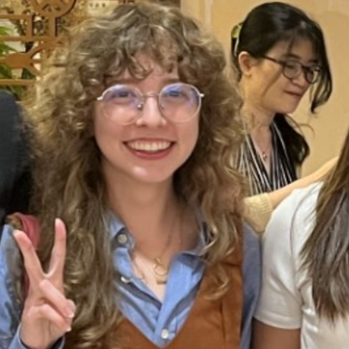 Woman with long brown curly hair giving a peace sign.