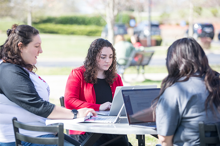 Three individuals sitting around a table and looking at laptop computers