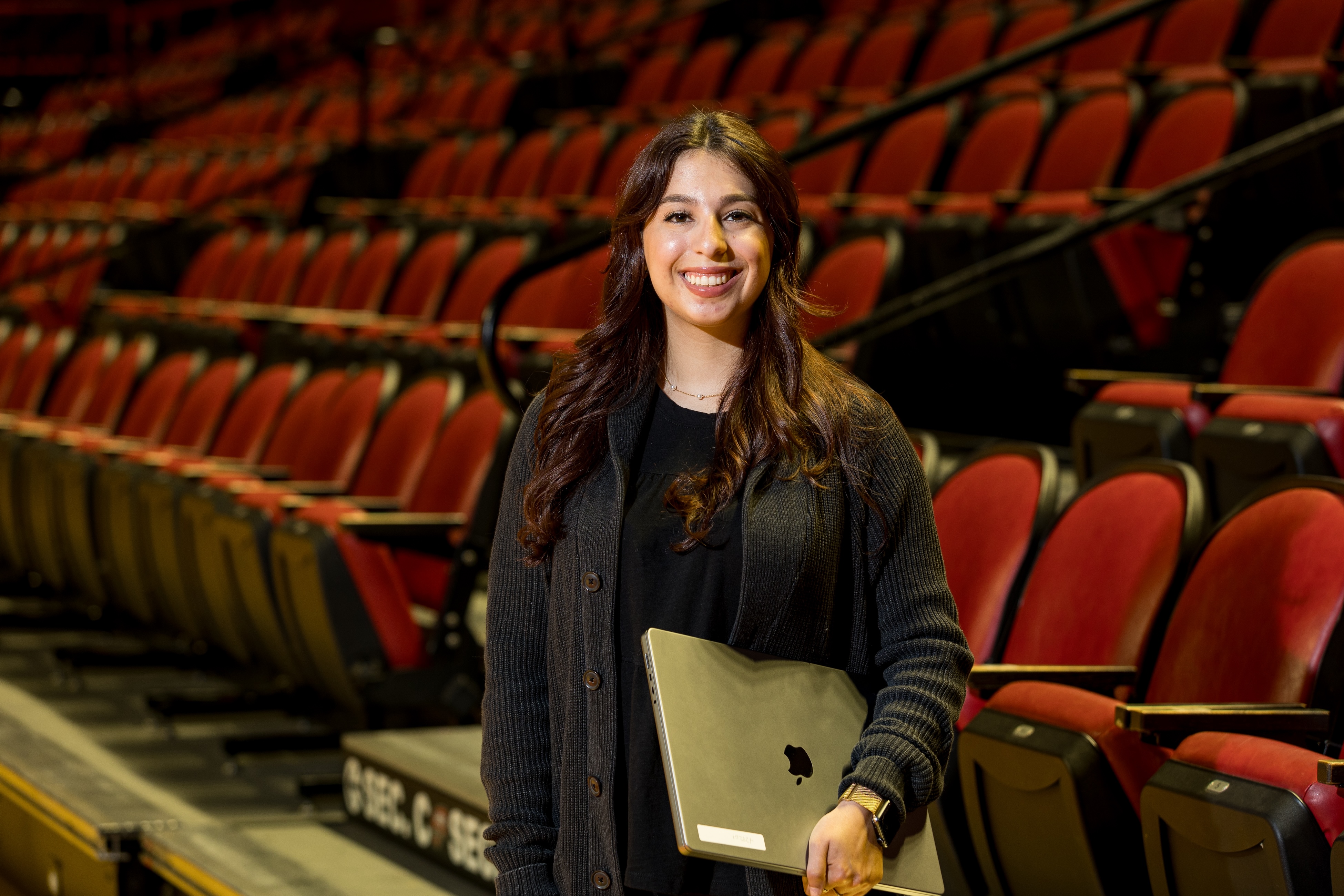 WKU student stands holding laptop in Diddle Arena