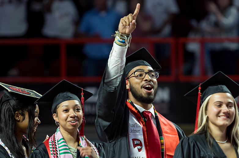 A group of School of Leadership and Professional Studies students walking at graduation. One student holds his pointer finger in the air to celebrate.