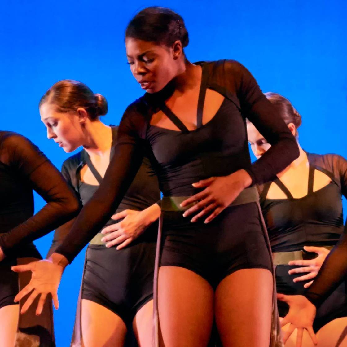 Women dancing looking stage left in soft dark blue and purple lighting.
