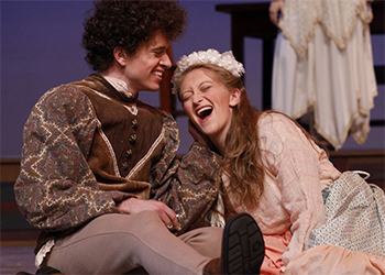 Man and woman sitting together on stage laughing.